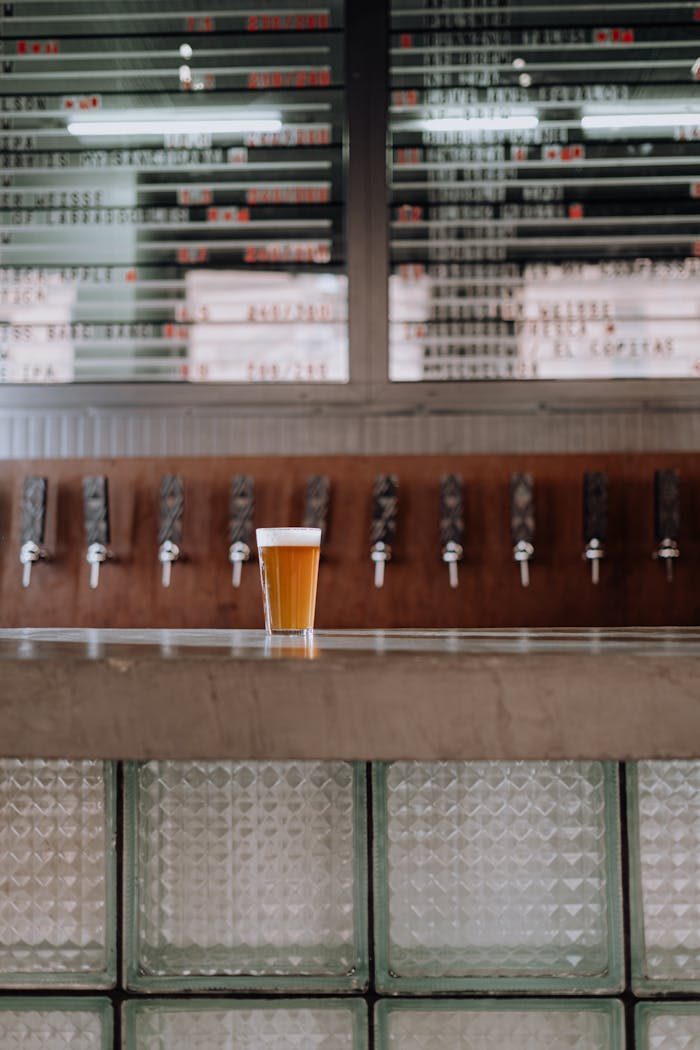 A single pint of craft beer sits on a sleek concrete bar in a contemporary pub with background taps.